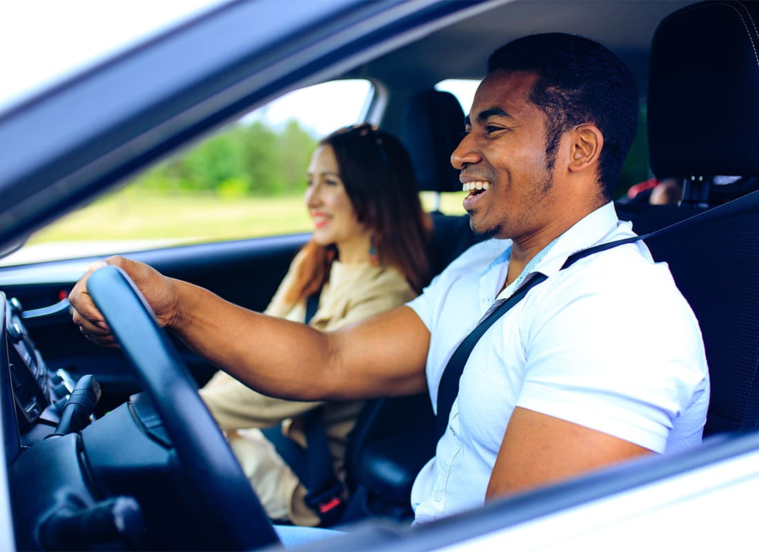 Personal Insurance - Portrait of a Cheerful Young Man Driving in a Car with his Wife Sitting Next to Him on a Warm Day